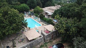A pool area with a stone building, surrounded by trees and a view of a village.