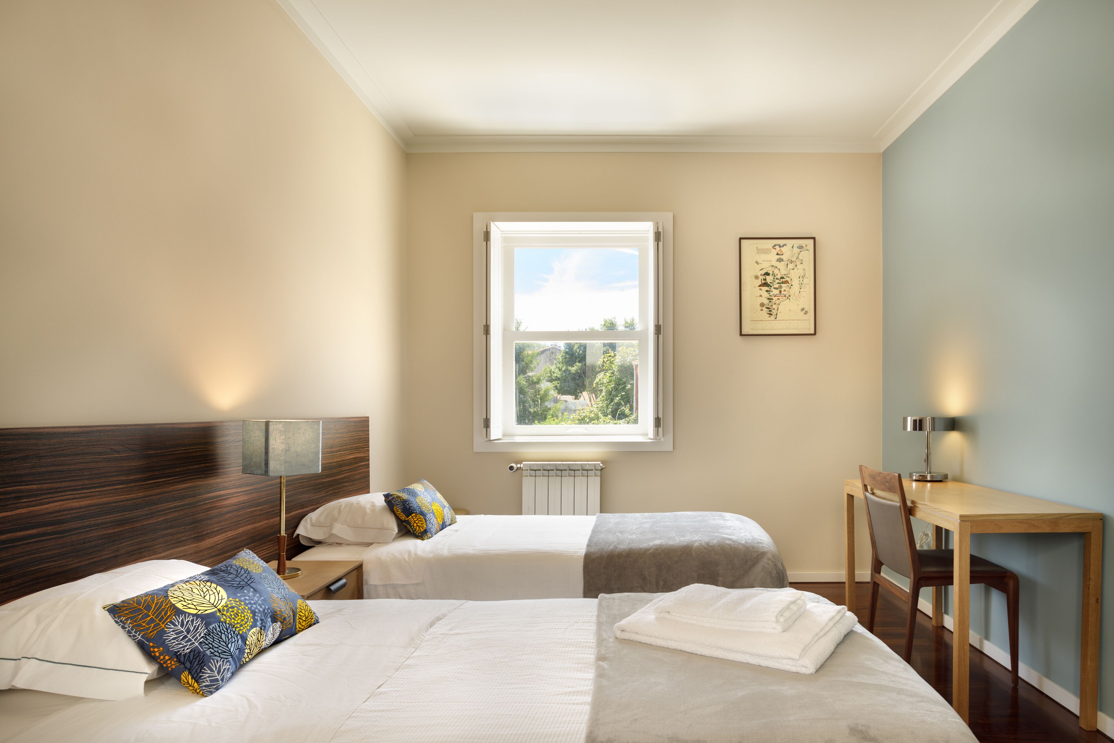 Camera d'albergo con due letti, una scrivania e una finestra vista verde.