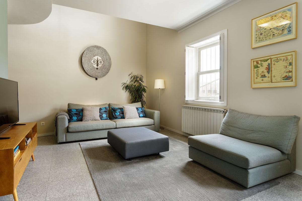A living room with a sofa, ottoman, and a television.
