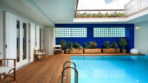 Piscina interior moderna con cubierta de madera, barandilla de vidrio y plantas en macetas.