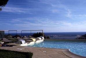 Un área de piscina con sillones de descanso y vista al océano.
