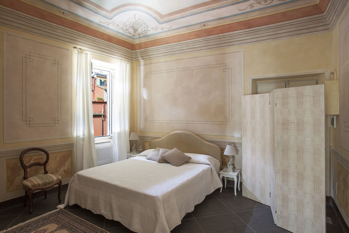 Un dormitorio con una cama grande, una silla, una mesita de noche y una puerta con cortina.