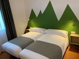 Cama doble con colcha de diseño geométrico, pared de acento verde, lámparas de noche y mesita con un teléfono.