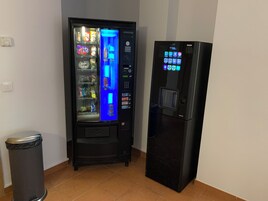Una máquina expendedora y un refrigerador en una habitación con piso de baldosas e interruptor de luz en la pared.