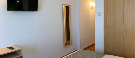 A hotel room with a bed, a TV mounted on the wall, a bedside table, and a wardrobe.