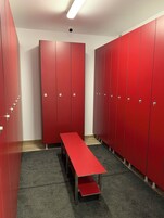 Un vestuario con taquillas rojas, un banco y una cámara de seguridad en el techo.