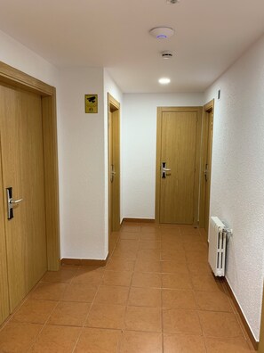 A hallway with wooden doors, a tiled floor, and a ceiling light. - Musher (Pas de la Casa)