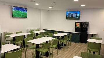 Un espace repas avec des tables et des chaises, un écran de télévision et un distributeur automatique.