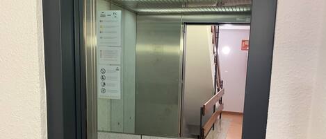 Interior de ascensor con acabado metálico, barandilla y suelo con diseño de rombos.