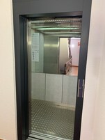 Interior de ascensor con acabado metálico, barandilla y suelo con diseño de rombos.