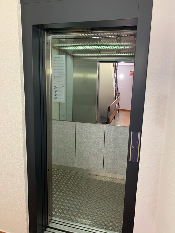 An elevator interior with a metallic finish, a handrail, and a floor with a diamond pattern. - Musher (Pas de la Casa)