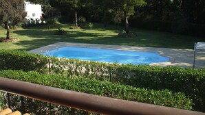 Ein rechteckiger Pool, umgeben von gepflegtem Rasen und Bäumen, mit einem weißen Gebäude im Hintergrund.