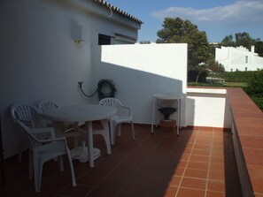 A patio with a white table and chairs, a small round table, and a garden hose.
