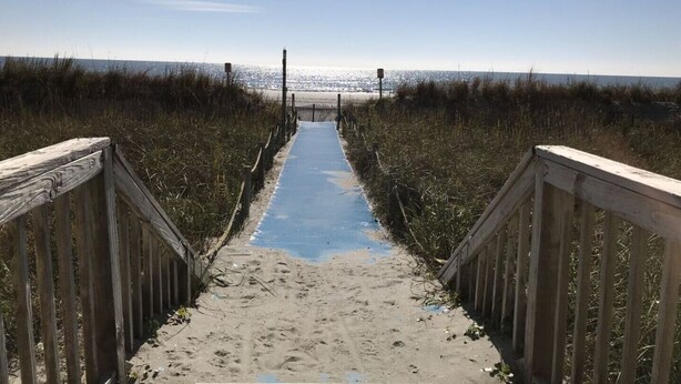 Un paseo marítimo de madera que conduce a la playa, con vista despejada al océano.