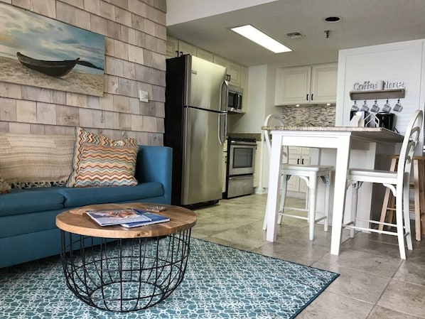 Una cocina moderna con armarios blancos, electrodomésticos de acero inoxidable y una zona de comedor con mesa y sillas blancas.