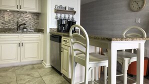 Una cocina con armarios blancos, una zona de café, un reloj y un comedor con sillas.