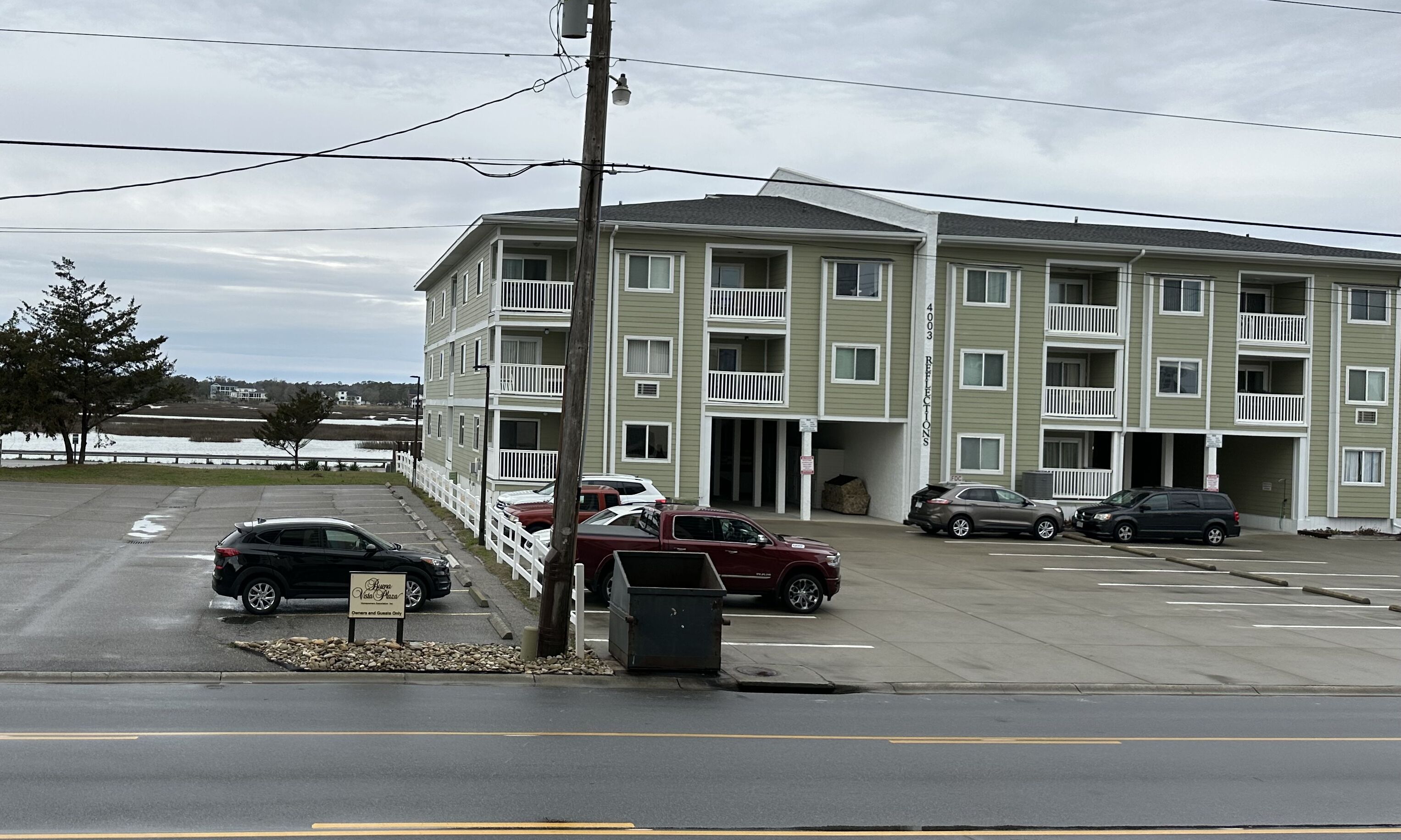 A multi-story apartment building with balconies, a parking lot, and a sign indicating a dining and lounge area.