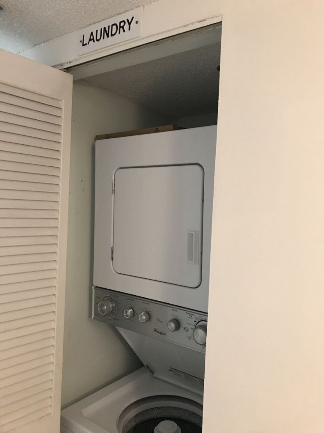A compact laundry room with a front-loading washer and dryer, a visible control panel, and a door labeled "LAUNDRY."
