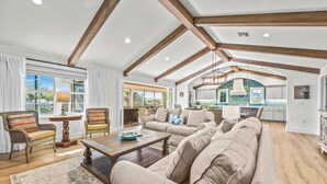 A spacious living room with a high ceiling, wooden beams, a large sofa set, a dining table, and a view to the kitchen. - Luxury Home with Pool and Dock for Fishing! (Anna Maria)