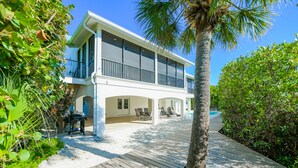 A two-story house with a balcony, a covered patio, and a wooden deck. - Luxury Home with Pool and Dock for Fishing! (Anna Maria)