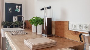 Cozinha com bancadas de madeira, pia, escorredor de louça, porta-facas, planta em vaso e cafeteira.