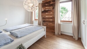 Quarto com cama, painel de parede de madeira, janela com cortinas e lustre.