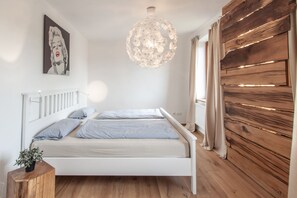 Ein Schlafzimmer mit einem weißen Bett, einem hölzernen Kopfteil, einer großen Kronleuchter und einer Wand mit Holzlatten.