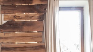 Um quarto com um separador de ripas de madeira, uma janela com cortinas e um radiador.