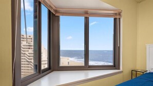 Quarto com uma grande janela panorâmica com vista para o mar, uma cama e uma pequena mesa.