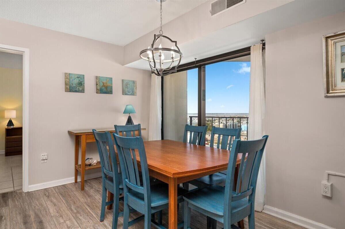 A dining area with a wooden table and blue chairs, a chandelier, and artwork on the wall.