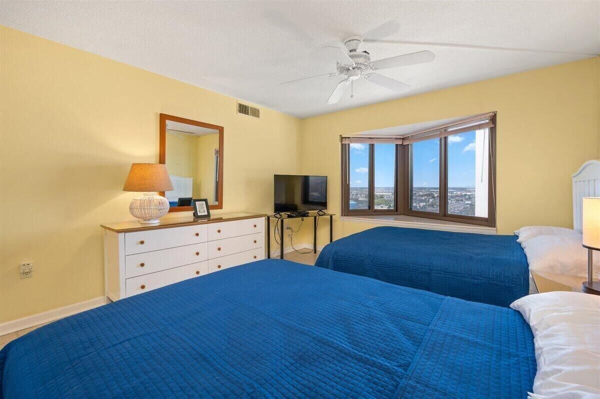 A hotel room with two beds, a ceiling fan, a TV, a dresser, and a window with a city view.