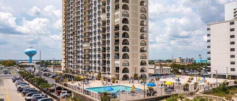 A high-rise hotel with a pool area, multiple balconies, and a view of the beach.