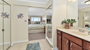A hotel room with a large bed, a bathroom with a mirror and sink, and a view of the sea through a sliding door. - Stunning Direct Ocean Front 3 Bedroom with Outdoor Pool! (Ocean City)