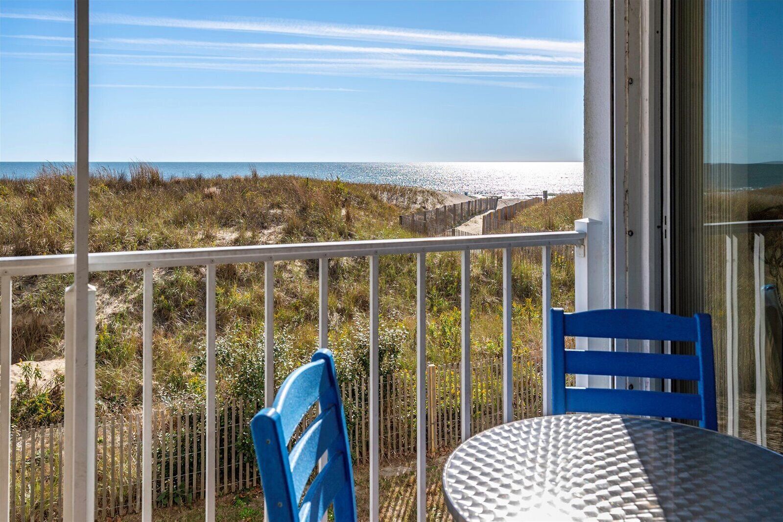 A balcony with a white railing, a blue chair, and a round table with a textured surface.