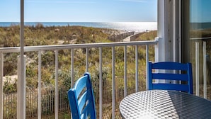 A balcony with a white railing, a blue chair, and a round table with a textured surface. - Stunning Direct Ocean Front 3 Bedroom with Outdoor Pool! (Ocean City)