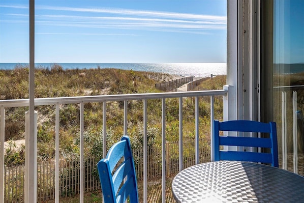 A balcony with a white railing, a blue chair, and a round table with a textured surface.