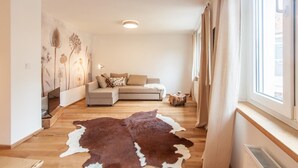 A modern living room with a sofa, a wooden floor, a cowhide rug, and a wall with botanical artwork. - Wohnen am Bäckerbrunnen (Würzburg)