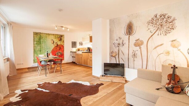A modern living room with a wooden floor, a cowhide rug, a sofa, a television, and a violin. - Wohnen am Bäckerbrunnen (Würzburg)