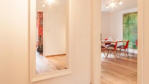 A modern interior with a wooden floor, a dining area with red chairs, and a large mirror on the wall. - Wohnen am Bäckerbrunnen (Würzburg)