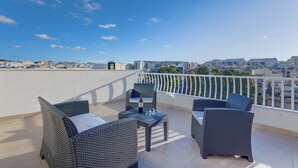 Terraço no telhado com móveis de vime, uma mesa e vista para a paisagem urbana.