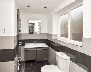 Ein modernes Badezimmer mit einem weißen Waschbecken, dunklen Fliesen und einem Fenster mit Blick.