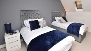 Une chambre avec deux lits, des murs gris, un radiateur blanc et un luminaire au plafond.