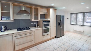 Une cuisine moderne avec des meubles en bois, une cuisinière à gaz, un four, un réfrigérateur et une fenêtre avec des stores.