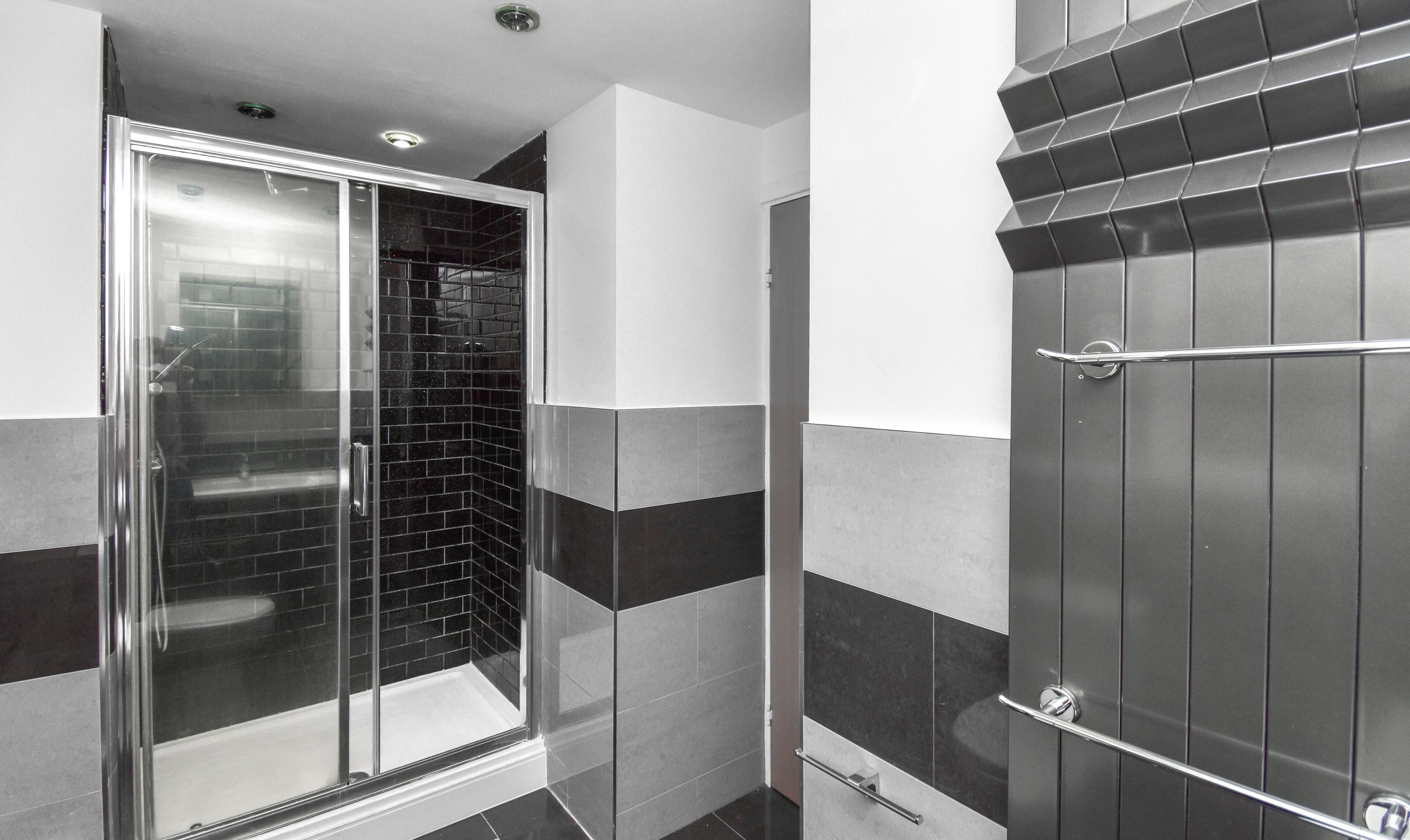 A modern bathroom with a glass shower enclosure, a dark tiled shower area, and a dark wooden door.
