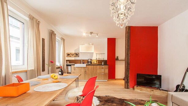 Un salon moderne avec un coin repas, une cuisine à l’arrière-plan et un mur d’accent rouge.