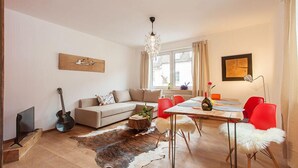 Un salon moderne avec un canapé, des fauteuils rouges, une table à manger et un lustre.