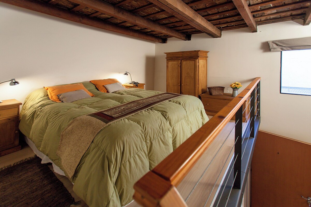 A bedroom with a bed, wooden headboard, nightstands, a wooden wardrobe, and a window with a view.