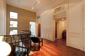 Un intérieur spacieux avec un parquet en bois disposé en chevrons, un escalier doté d’une rampe noire et une vue sur l’extérieur par une fenêtre.