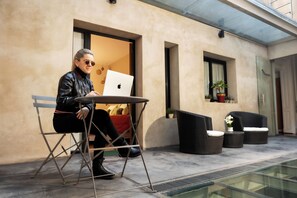 Eine Person sitzt an einem Tisch mit einem Laptop vor einem Gebäude mit Glasboden, einem Blumentopf und einer Tür.
