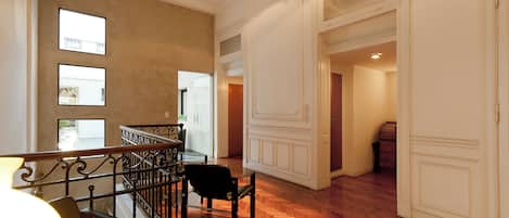 A spacious interior with a wooden herringbone floor, a staircase with a black railing, and a view of the outside through a window.
